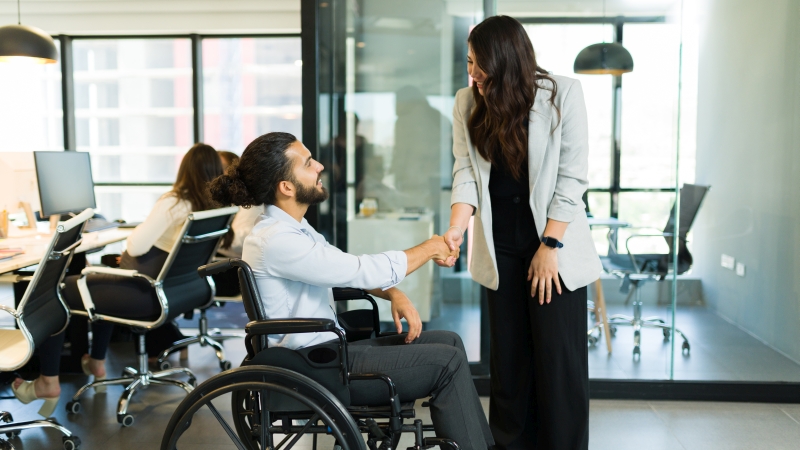 Geschäftsmann im Rollstuhl schüttelt Geschäftsfrau im Büro die Hand