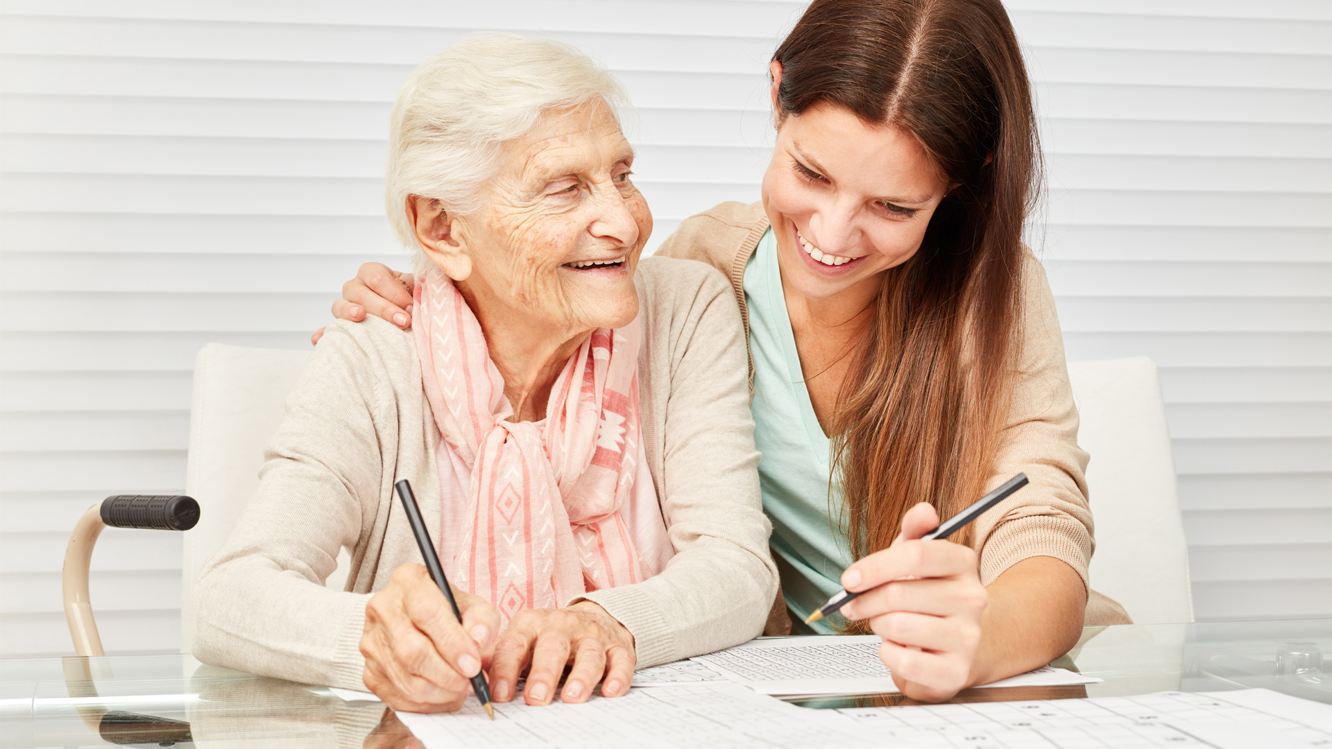 Junge Person hilft lächelnd einer älteren Person beim Ausfüllen von Formularen.